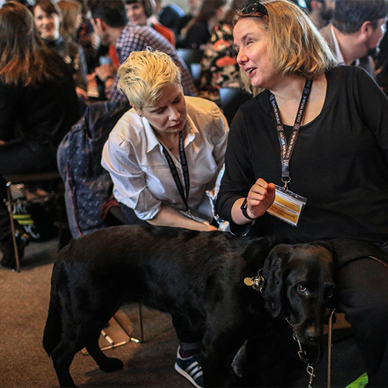 TWo people in discussion at Access All Areas event with guide dog