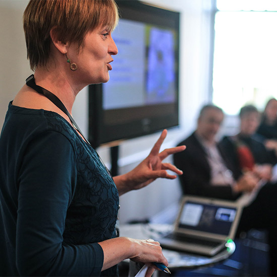 A woman delivering a workshop with panel of people in background